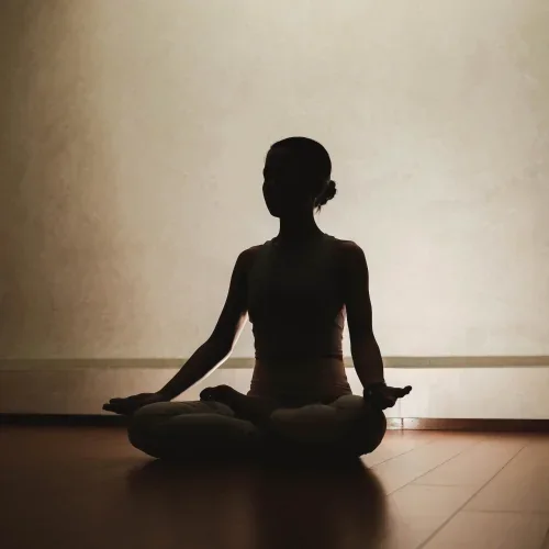Silhouette di una persona seduta in meditazione in una stanza in penombra